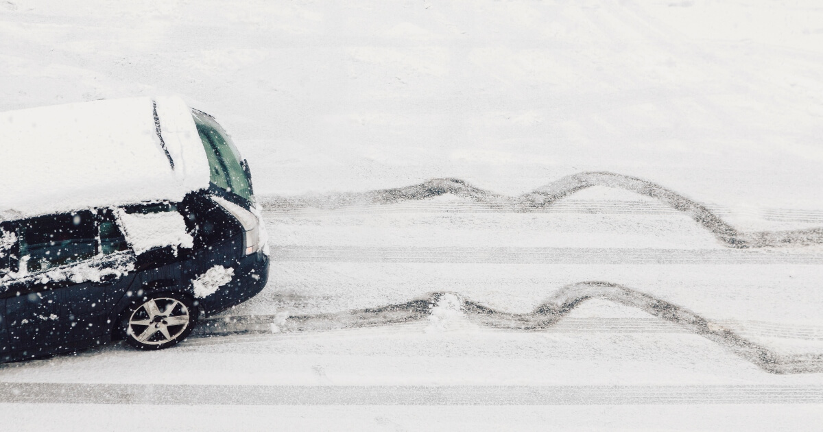 Snowy image of the back end of a black SUV skidding across a snow-covered road